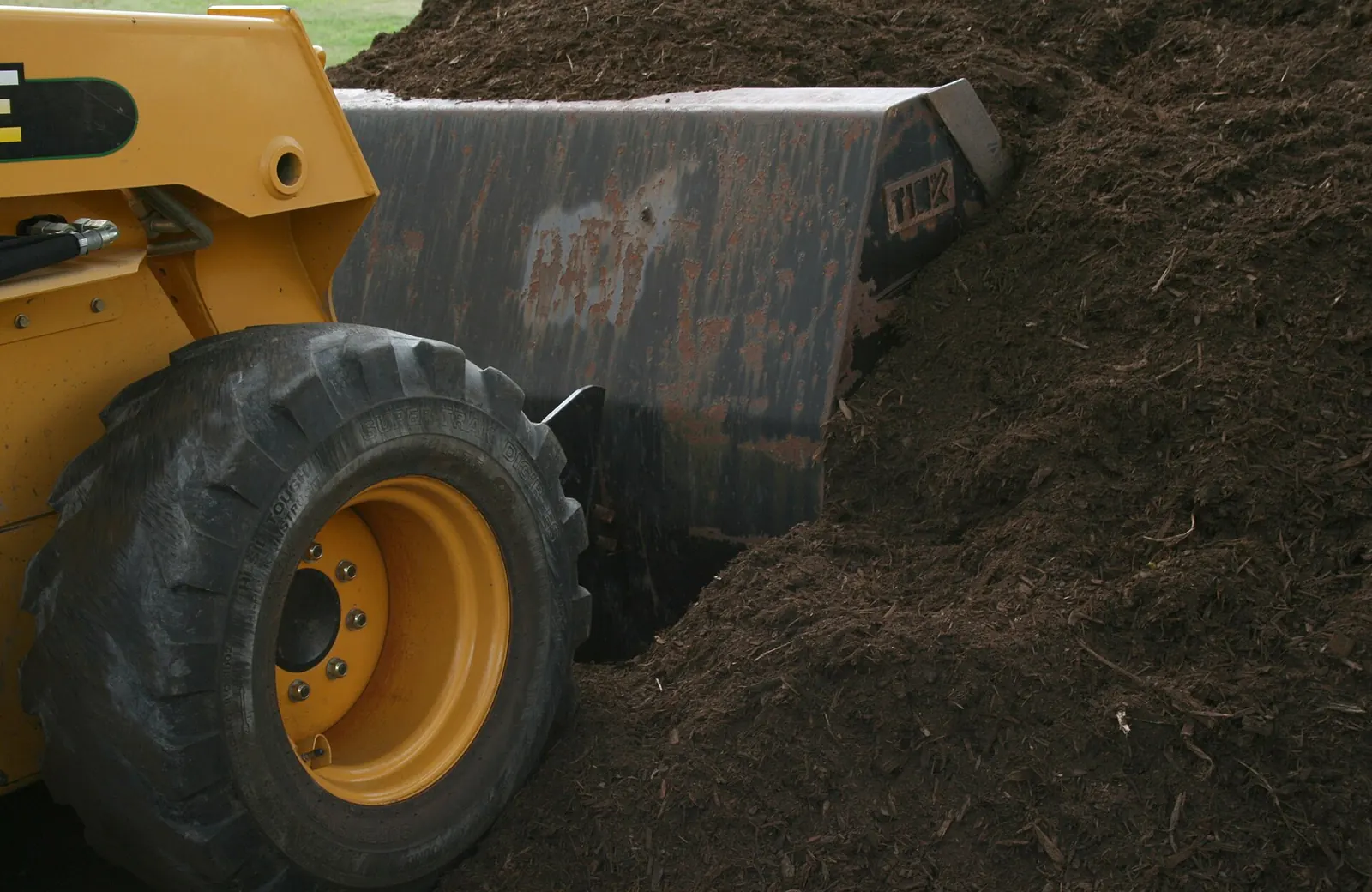 A loader bucket working a large pile of wood mulch